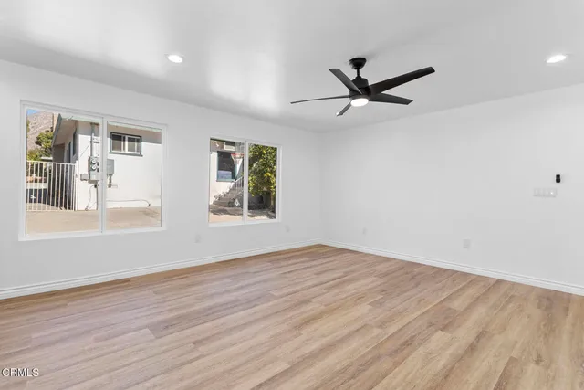 an empty room with wooden floor fan and windows