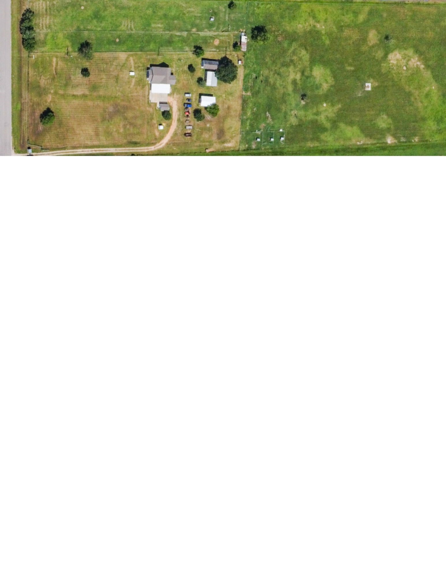 11301 South FM 441 Road El Campo, TX 77437 - Photo 8 of 43 Aerial view of a spacious 10 acre rural property. It features a large, open field with a few trees, a house, guest house, and several outbuildings. The property is accessible by paved FM road.