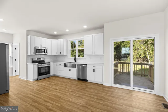 a kitchen with granite countertop a refrigerator oven a sink and white cabinets with wooden floor