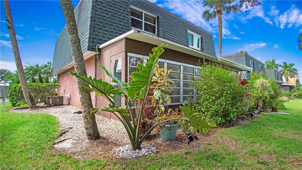 600 Valley Stream Drive, Unit C1 Naples, FL 34113 - Photo 28 of 44 Rear view of house featuring mansard roof, a lawn, and brick siding