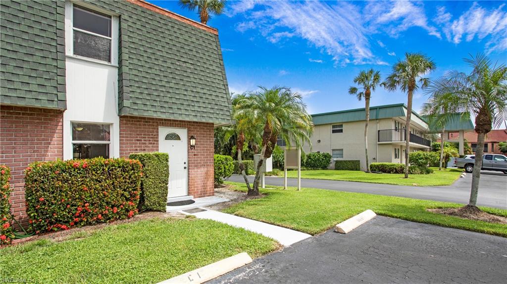600 Valley Stream Drive, Unit C1 Naples, FL 34113 - Photo 29 of 44 View of front facade with mansard roof, a shingled roof, brick siding, a front lawn, and uncovered parking