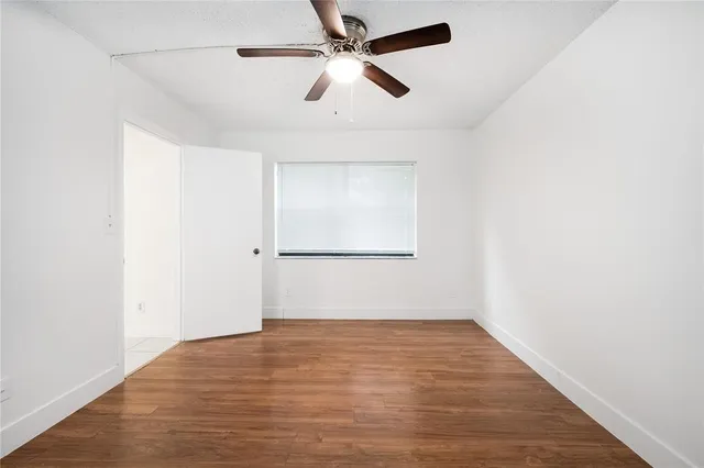 an empty room with wooden floor ceiling fan and windows