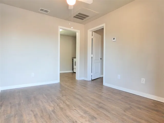 a view of an empty room with wooden floor and a ceiling fan