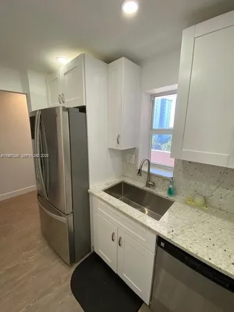 a kitchen with stainless steel appliances granite countertop a refrigerator a sink and white cabinets