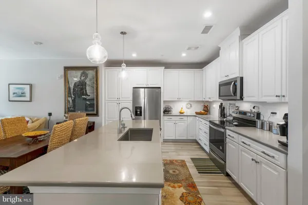 a large white kitchen with stainless steel appliances granite countertop a stove a sink a refrigerator white cabinets and wooden floor