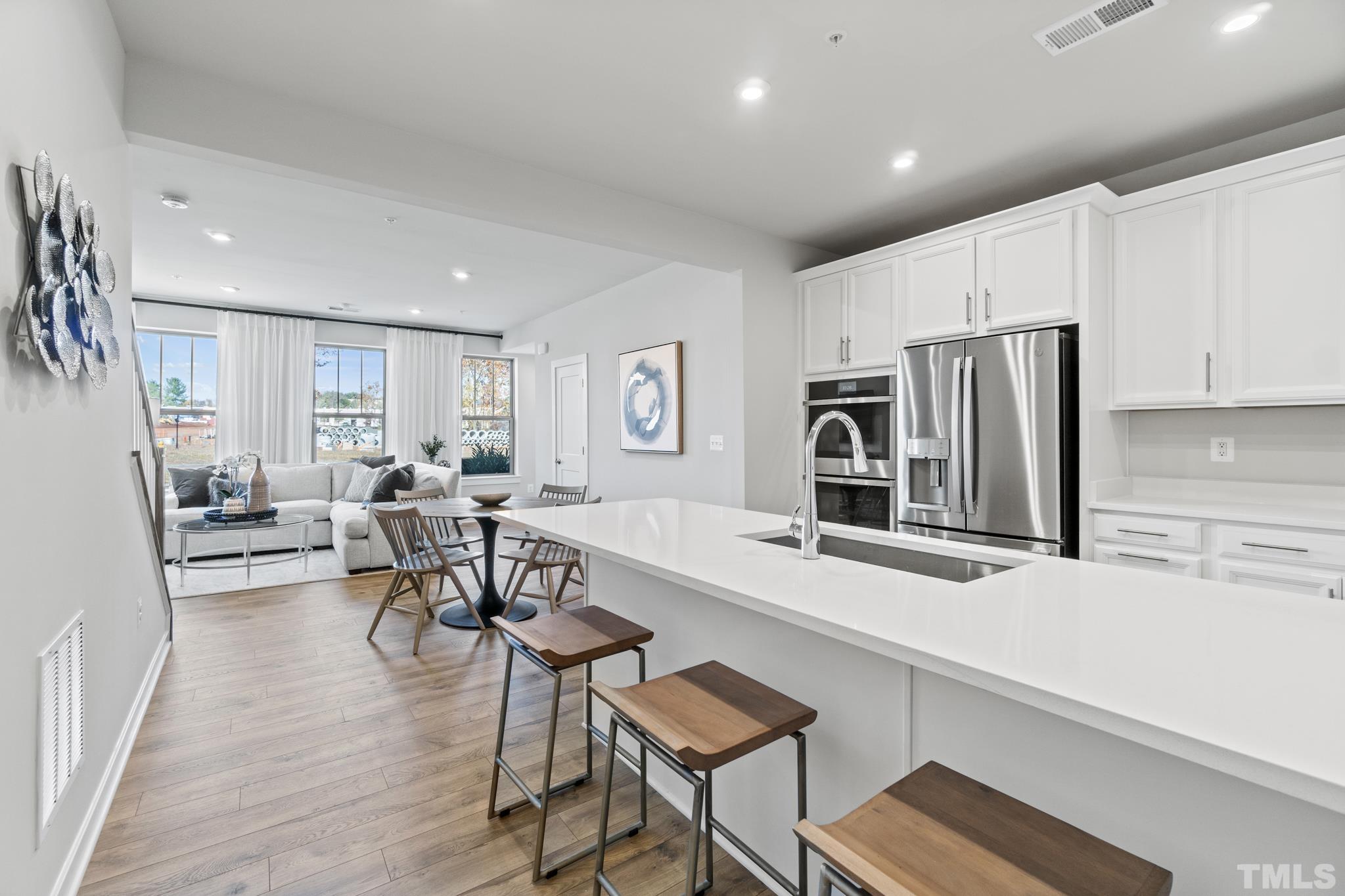 a living room with stainless steel appliances furniture a flat screen tv and a refrigerator