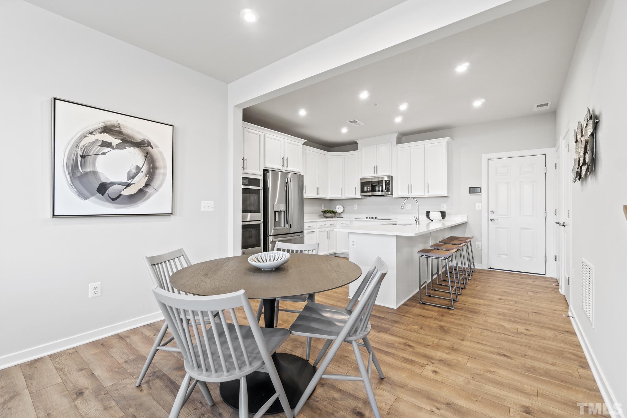 415 Wait Avenue, Unit 100 TESSA Wake Forest, NC 27587 - Photo 4 of 29 a kitchen with stainless steel appliances kitchen island granite countertop a dining table chairs and refrigerator