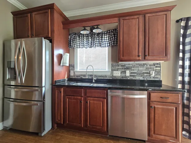 a kitchen with stainless steel appliances granite countertop wooden cabinets a refrigerator a stove a sink and dishwasher with wooden floor