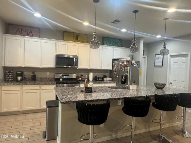 a kitchen with stainless steel appliances granite countertop a sink a stove a microwave a refrigerator and chairs