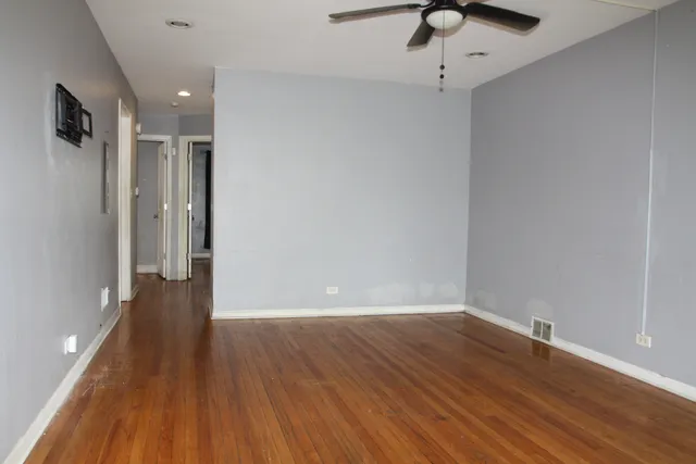 a view of an empty room with wooden floor and a ceiling fan