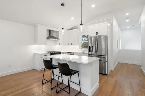a kitchen with stainless steel appliances granite countertop a refrigerator a sink dishwasher a stove and white cabinets with wooden floor