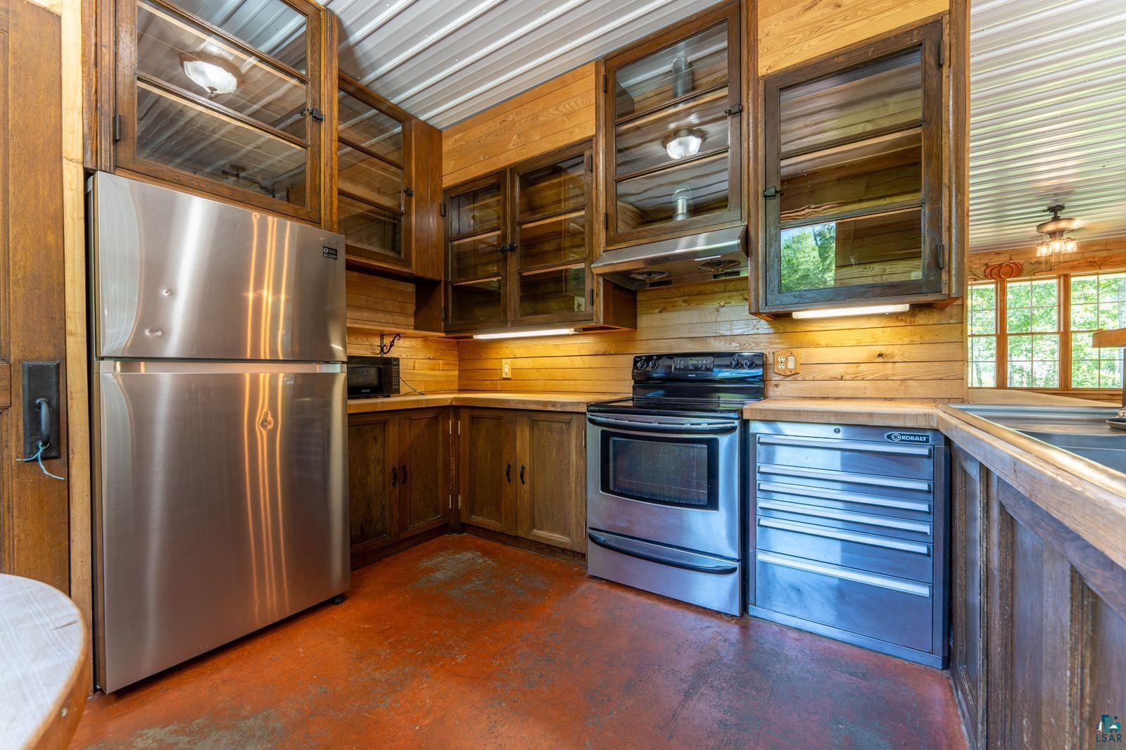 9734 Alango Road Angora, MN 55703 - Photo 8 of 41 Kitchen featuring stainless steel appliances, wood-finish cabinetry with glass inserts, wood-finish shiplap walls, and a corrugated metal ceiling