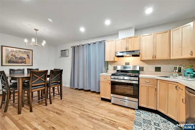 a kitchen with stainless steel appliances granite countertop a stove a refrigerator a sink a dining table and chairs with wooden floor