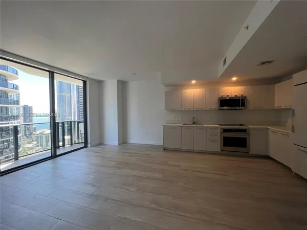 a view of an empty room with kitchen view and a large window