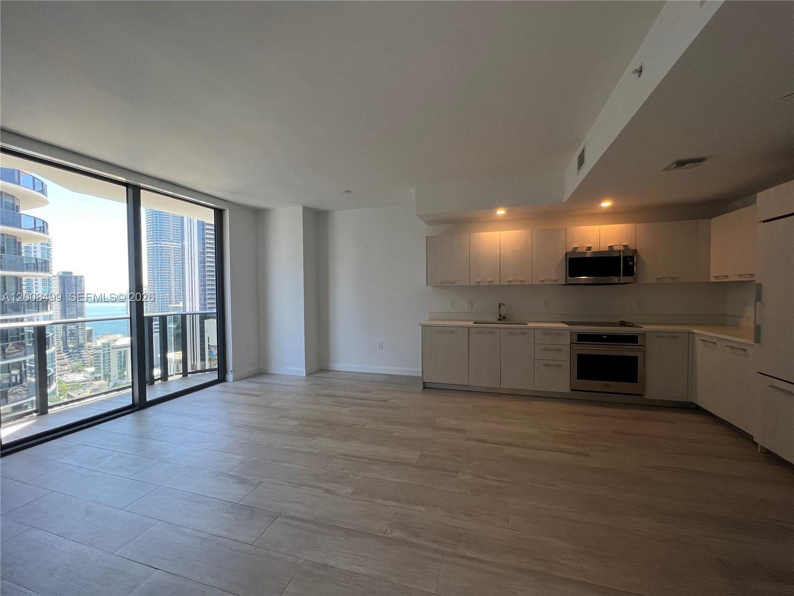 a view of an empty room with kitchen view and a large window