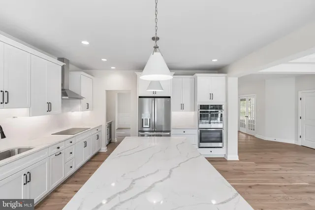a kitchen with stainless steel appliances kitchen island granite countertop a refrigerator oven stove a sink dishwasher and white cabinets with wooden floor