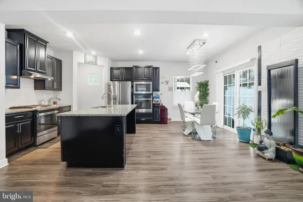 a living room with stainless steel appliances kitchen island granite countertop a stove top oven a sink dishwasher a dining table and chairs with wooden floor