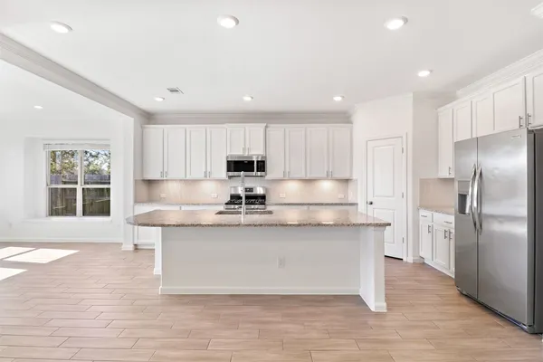 a large kitchen with stainless steel appliances a large counter top a stove a refrigerator and white cabinets