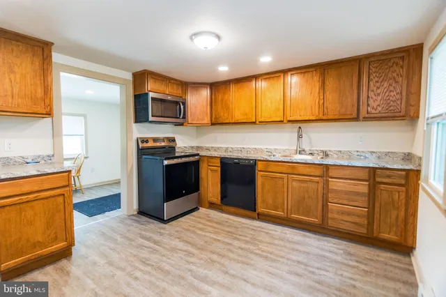 a kitchen with stainless steel appliances granite countertop wooden cabinets a stove top oven a sink and dishwasher with wooden floor
