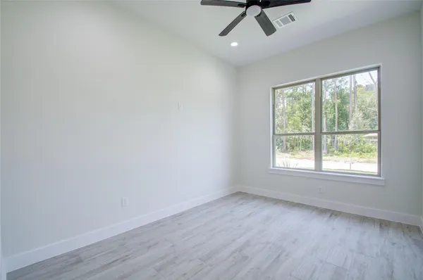 an empty room with wooden floor fan and windows