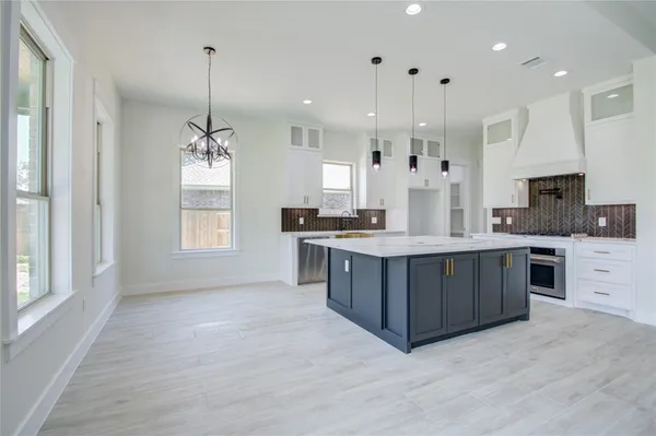a large kitchen with stainless steel appliances kitchen island granite countertop a stove a sink a refrigerator and white cabinets with wooden floor