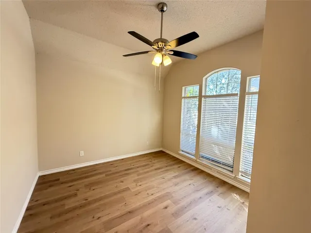 an empty room with wooden floor fan and windows