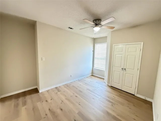 an empty room with wooden floor fan and windows