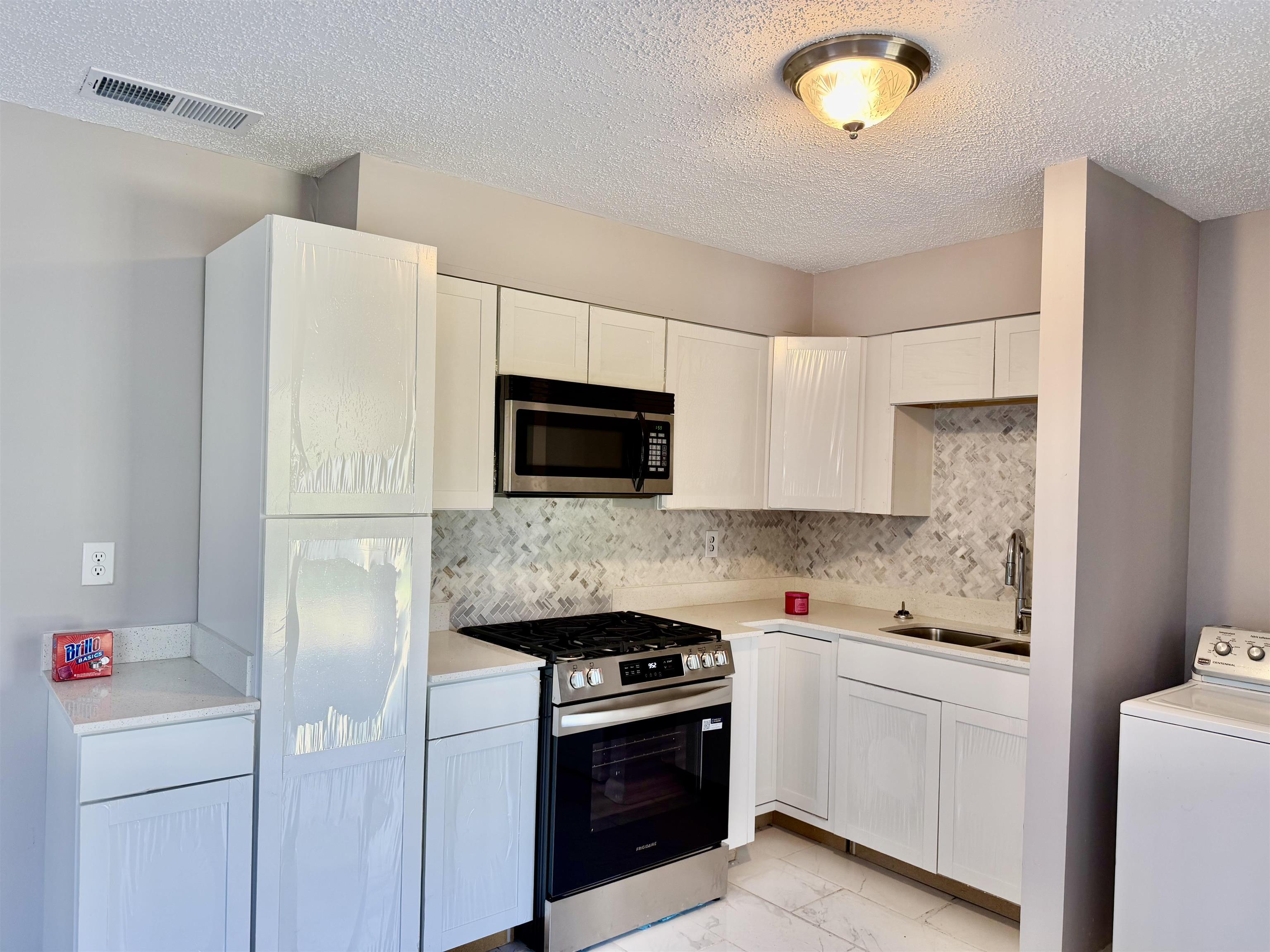 2215 Henrietta Road Memphis, TN 38134 - Photo 2 of 10 Kitchen featuring washer / clothes dryer, stainless steel appliances, white cabinets, a textured ceiling, and tasteful backsplash