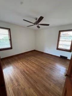 an empty room with wooden floor fan and windows