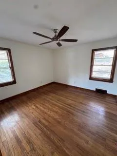 an empty room with wooden floor fan and windows