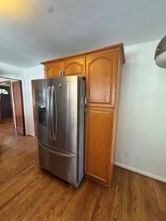 a view of a refrigerator in kitchen and an empty room with wooden floor