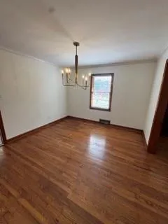an empty room with wooden floor chandelier and windows