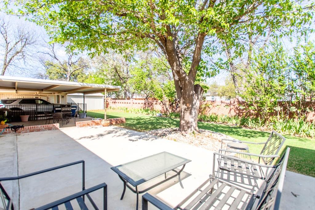 149 Russ Street Albany, TX 76430 - Photo 22 of 25 a view of a patio with table and chairs under an umbrella with large trees