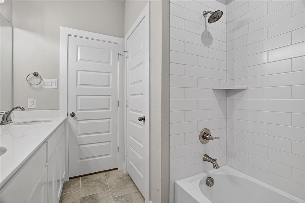 504 Clifton Court Springtown, TX 76082 - Photo 23 of 36 Full bathroom featuring a white subway tile tub surround with an integrated corner shelf, brushed nickel fixtures, a white vanity with an undermount sink, and a coordinating countertop