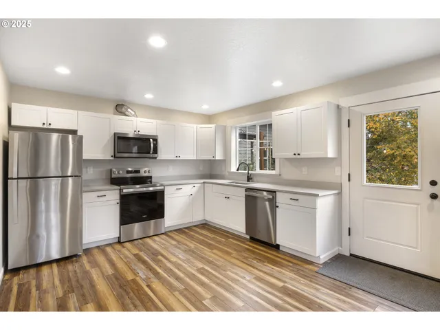 a kitchen with granite countertop a refrigerator oven a sink dishwasher and white cabinets with wooden floor