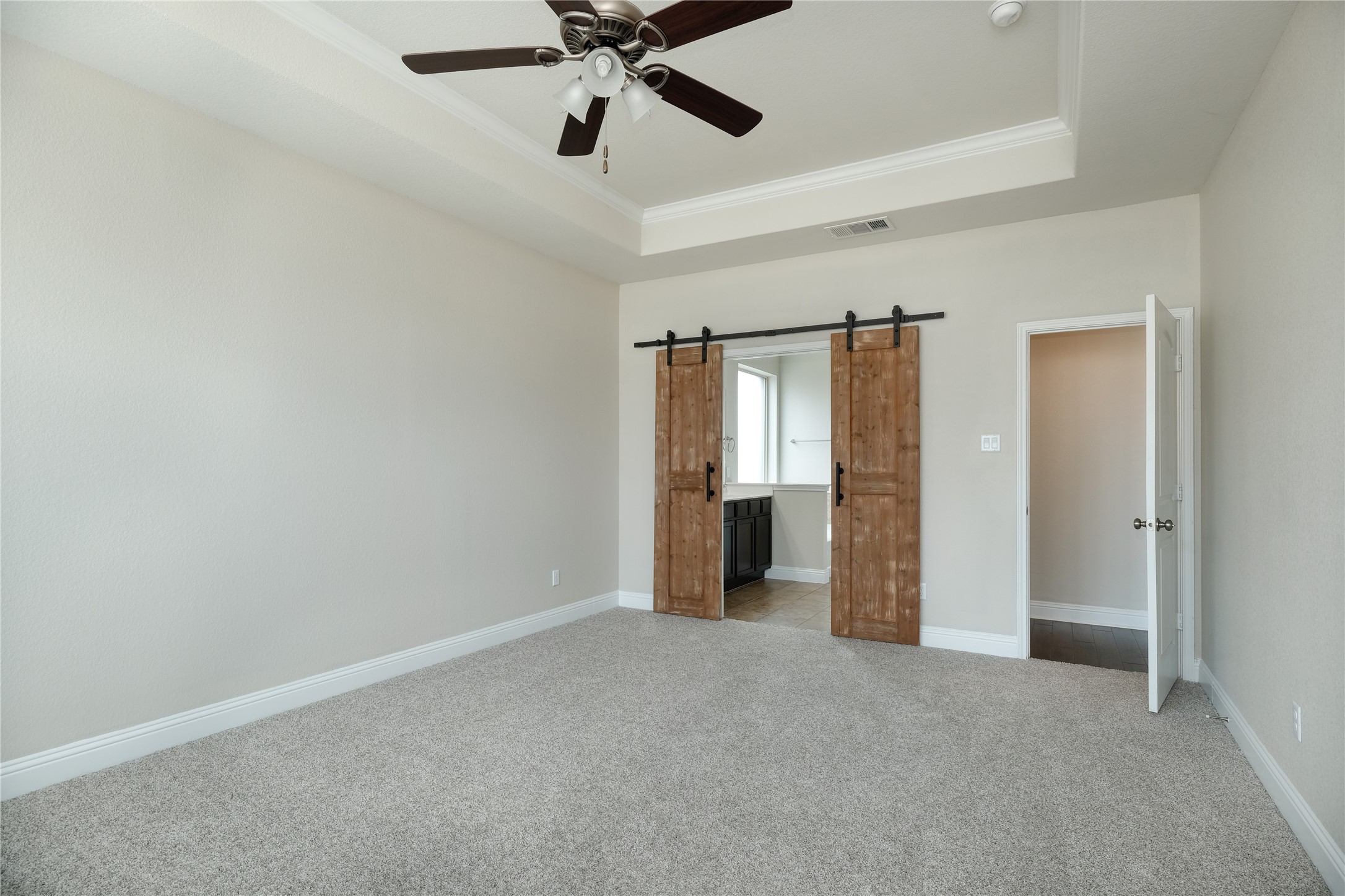 1804 Elaina Loop Leander, TX 78641 - Photo 4 of 12 Unfurnished bedroom with a barn door, crown molding, light colored carpet, a tray ceiling, and a ceiling fan