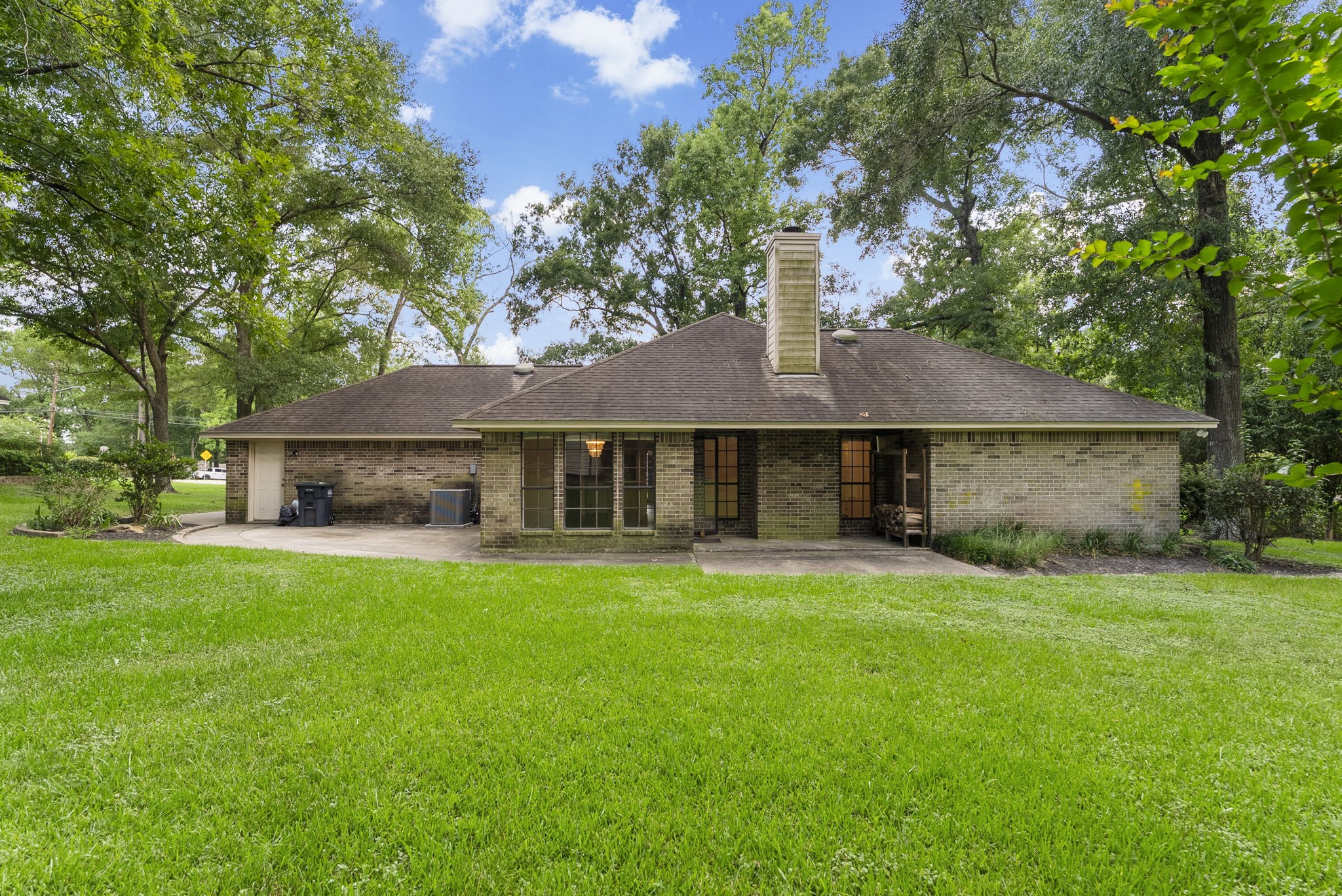 202 Sunset Boulevard Conroe, TX 77303 - Photo 39 of 50 Charming single-story brick home with a spacious backyard, surrounded by mature trees. Features a cozy chimney and large windows, offering plenty of natural light. Ideal for those seeking a serene and inviting outdoor space.