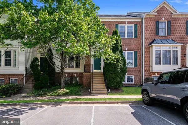 a view of a brick house with a yard plants and a large tree