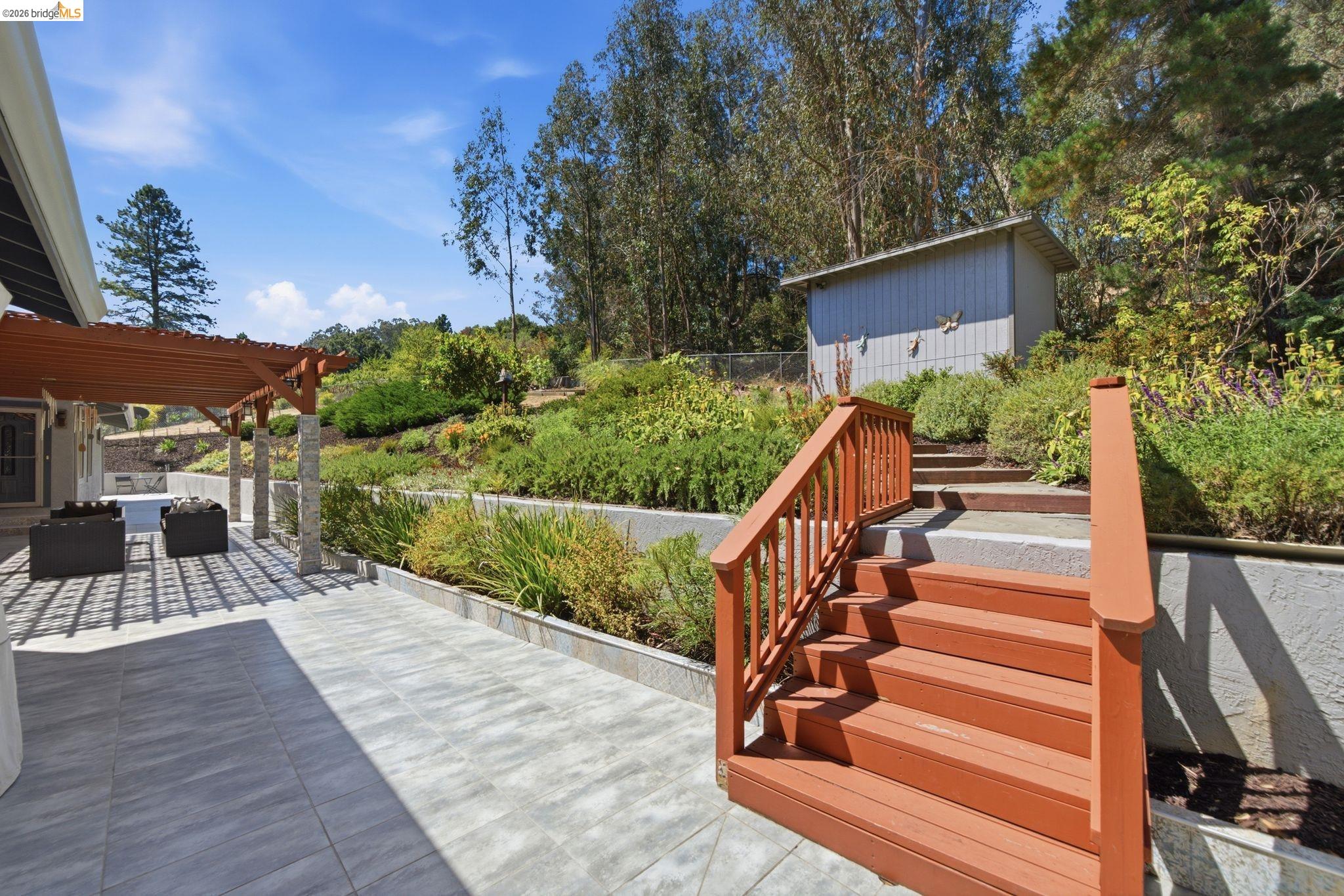11133 Golf Links Road Oakland, CA 94605 - Photo 47 of 57 Expansive outdoor patio featuring large format tile, a wood pergola with stone-wrapped columns, and a terraced hillside with mature landscaping