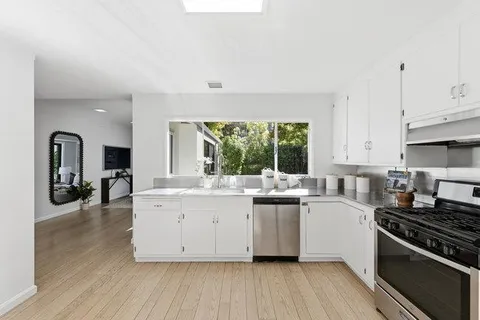 a kitchen with stainless steel appliances granite countertop a stove top oven a sink dishwasher and a refrigerator with wooden floor