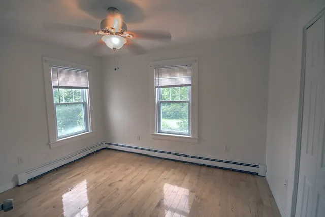an empty room with wooden floor fan and windows