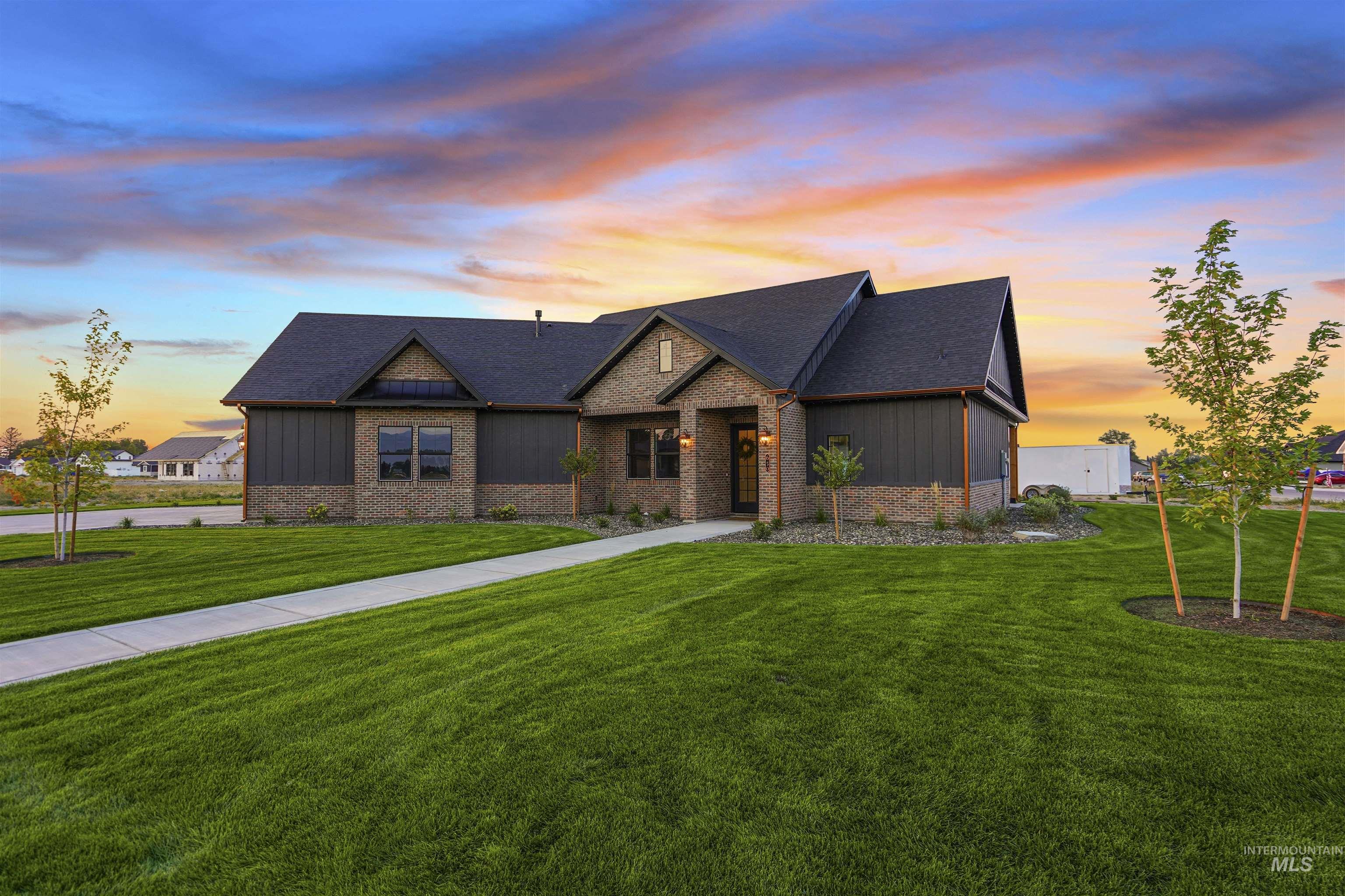 View of front of house with board and batten siding, a lawn, a shingled roof, and brick siding