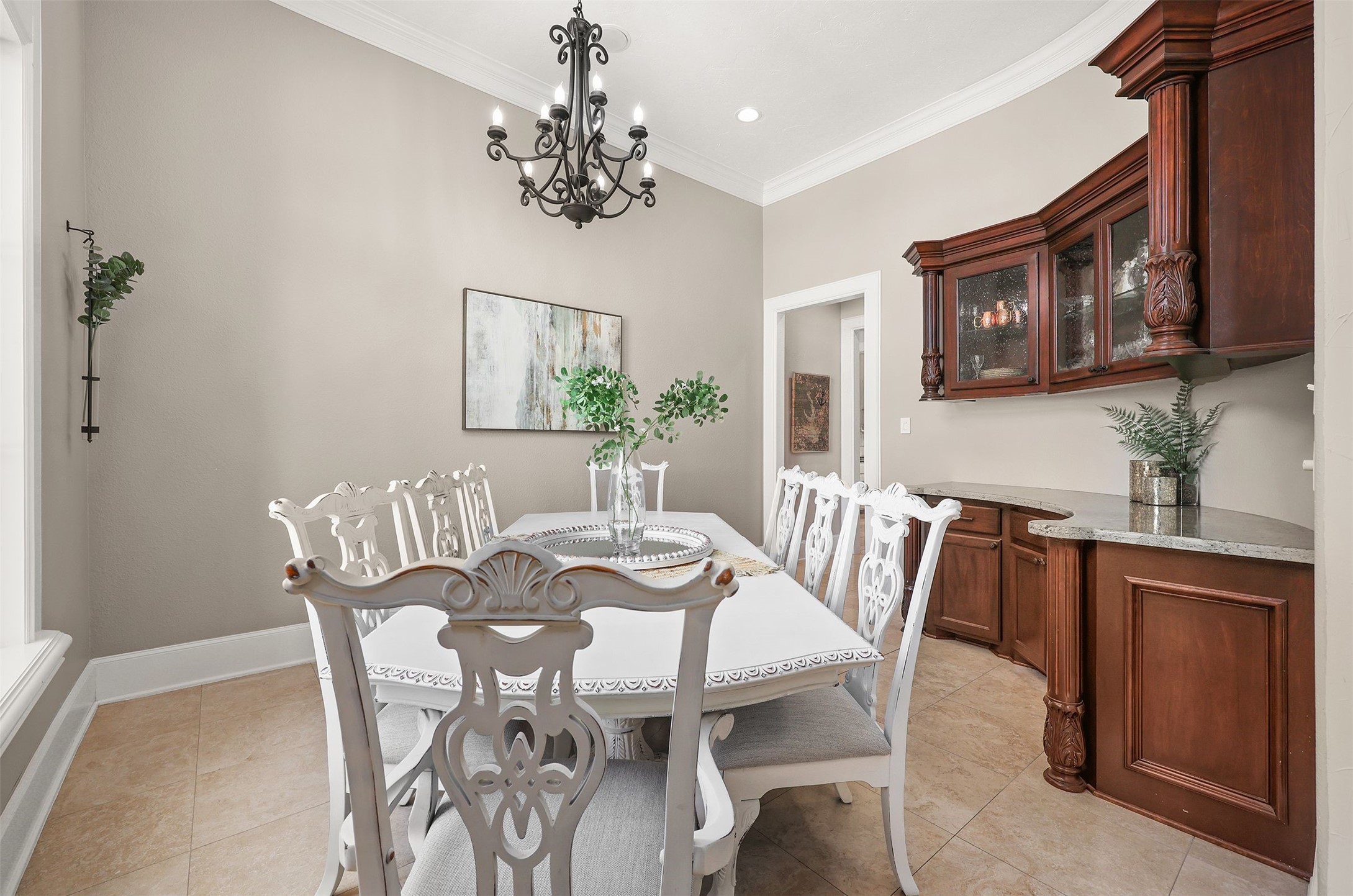 10896 Decatur Street Willis, TX 77318 - Photo 17 of 50 This elegant dining room boasts a classic chandelier, a large table with ornate white chairs, warm-toned walls, and a built-in wooden cabinet for ample storage, all beautifully accented with tasteful artwork and greenery.