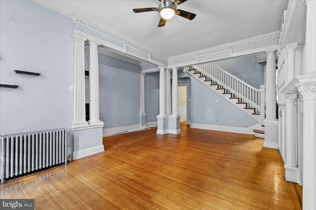 a view of an empty room with wooden floor and a ceiling fan