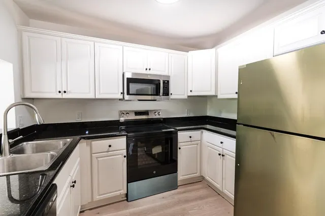 a kitchen with granite countertop a refrigerator sink and white cabinets