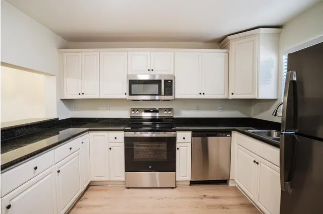 a kitchen with granite countertop white cabinets sink and stainless steel appliances