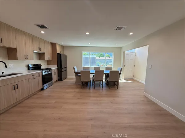 a kitchen with stainless steel appliances granite countertop a stove top oven a sink dishwasher a dining table and chairs with wooden floor