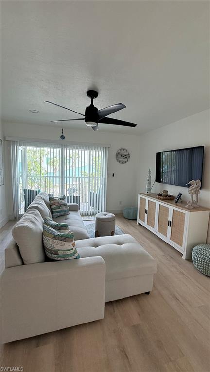 Bright living space featuring wood-finish flooring, a contemporary ceiling fan, and sliding glass doors with vertical blinds