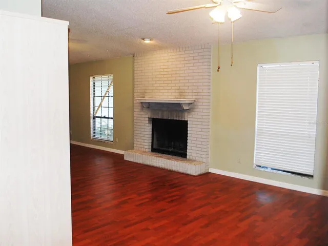 an empty room with wooden floor fireplace and windows