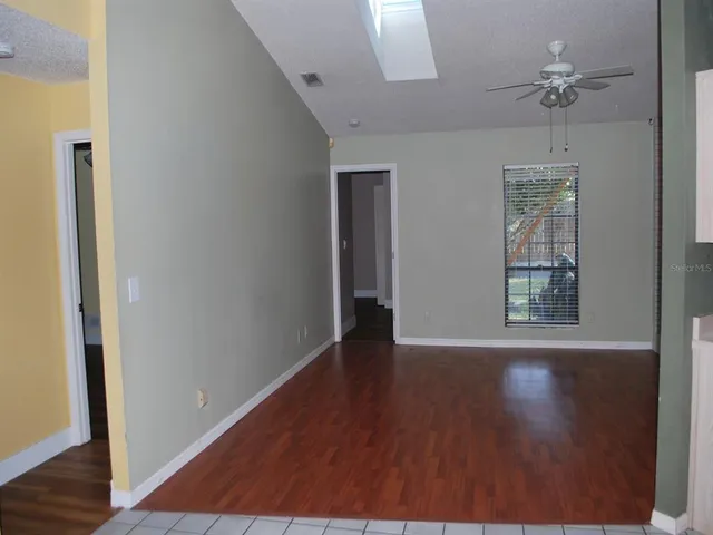 an empty room with wooden floor chandelier fan and windows